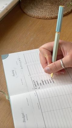 a person holding a pen and writing on a piece of paper that is sitting on a desk