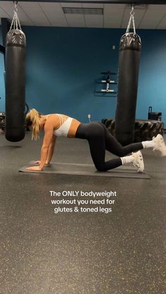 a woman is doing push ups on a mat in a gym with two punching bags