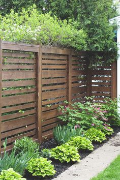 a wooden fence in the middle of a yard with plants growing on top of it