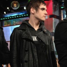 a young man in a leather jacket standing next to another person wearing a hoodie