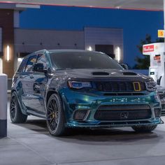 a blue jeep is parked in front of a gas station at night with its lights on