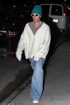 a man in white sweater and blue jeans walking down the street with his skateboard