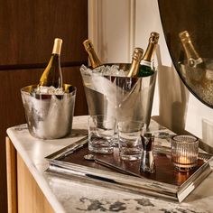 three bottles of champagne in ice buckets on a marble counter top next to a mirror