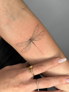 a woman's arm with a small dragonfly tattoo on the left side of her arm