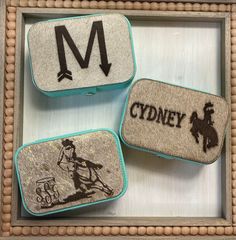 three magnets with different designs on them sitting in a wooden frame, one has an m and the other is a cowboy