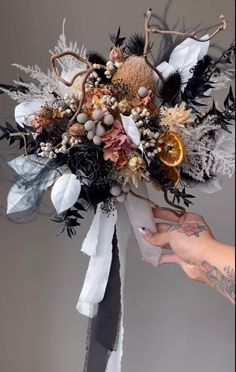 a person is holding a bouquet with flowers and feathers on it in front of a gray background