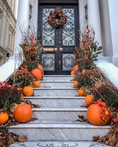 a set of steps with pumpkins and flowers on the bottom, in front of a door