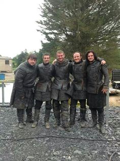 a group of men standing next to each other on top of a gravel covered field