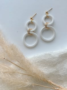 two white circular earrings sitting on top of a feather