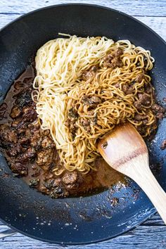 a skillet with noodles, meat and sauce being stirred by a wooden spatula