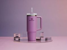 a purple travel mug with a straw in it on a clear stand against a pink background