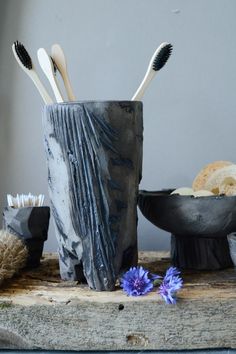 three toothbrushes are in a cup on a table next to some bowls with flowers