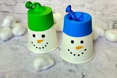 two snowmen made out of plastic cups sitting on a marble counter with cotton balls