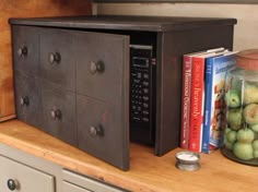 a microwave oven sitting on top of a wooden counter next to books and cans filled with apples