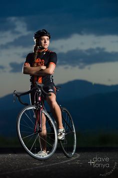 a woman is posing with her bike on the road at night, wearing an orange shirt and black shorts