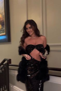 a woman in a black sequin dress standing next to a stair railing and smiling at the camera