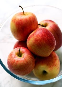 four red apples in a glass bowl on a marble counter top, with the tops slightly down