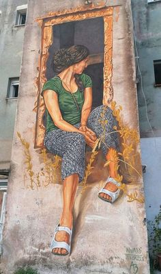 a mural on the side of a building depicts a woman sitting in a window with her feet up