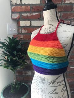 a mannequin wearing a multicolored crochet halter top next to a potted plant