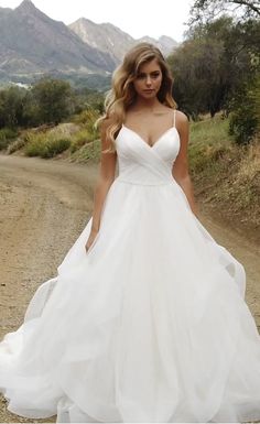 a woman in a white wedding dress walking down a dirt road