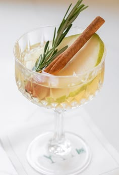 an apple and cinnamon drink in a wine glass with rosemary garnish on the rim