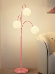 a pink floor lamp with four white balls on it's base and a couch in the background