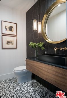 a bathroom with black and white tile, gold framed pictures, and a round mirror