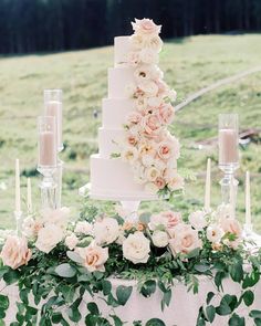 a wedding cake with flowers and candles on the table in front of an open field