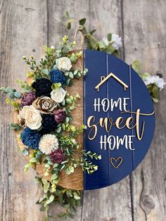 a sign that says home sweet home with flowers and greenery around it on a wooden surface