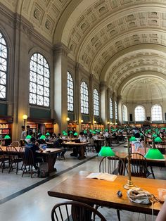 people are sitting at tables and reading books in a large room with high ceilinged ceilings