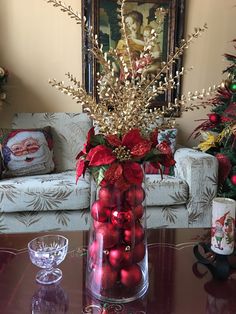 a glass vase filled with red balls on top of a table next to a christmas tree