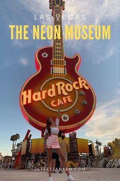 a woman standing in front of a neon rock cafe sign with the words hard rock cafe on it