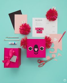 a pink box with red pom poms on top of it next to scissors and other items