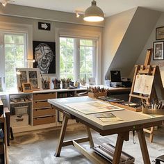 an artist's studio with lots of art supplies on the desk and in front of two large windows