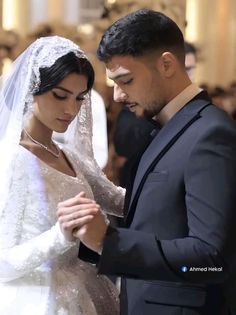 the bride and groom are looking down at their wedding dress while they stand in front of an audience