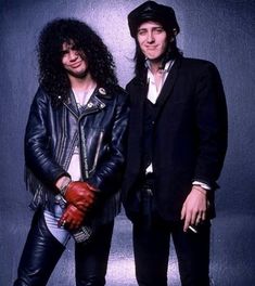 two men standing next to each other in front of a blue wall wearing leather gloves