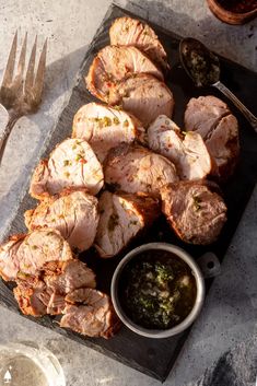 some meat is sitting on a cutting board next to a knife and fork with sauce in it