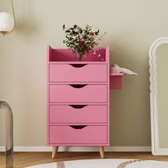 a pink dresser with flowers in it next to a mirror and lamp on the floor