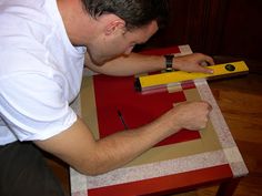 a man is cutting paper with a pair of scissors on a piece of red and yellow cardboard