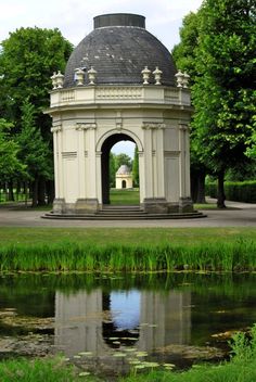 a gazebo sitting in the middle of a lush green park next to a pond