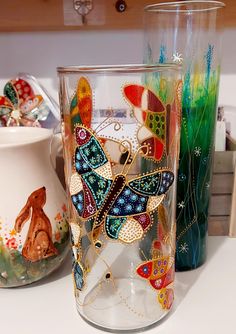 two glass vases sitting on top of a counter next to each other, one with a butterfly painted on it