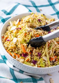 a white bowl filled with coleslaw and carrots next to a pair of tongs