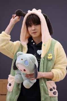 a person holding a stuffed animal in front of their face and wearing a green jacket