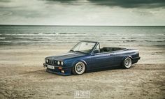 a blue convertible car parked on top of a sandy beach next to the ocean under a cloudy sky