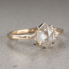 a three stone diamond ring on top of a gray surface, with two smaller diamonds in the middle