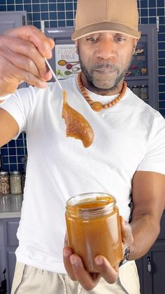 a man holding a jar of peanut butter and spoon in his right hand while wearing a hat