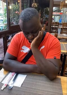 a man sitting at a table talking on a cell phone and holding his hand to his face