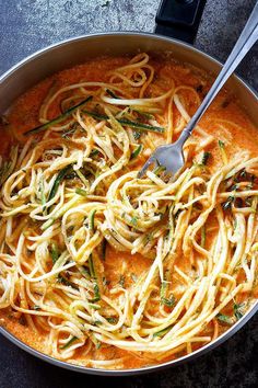 a pan filled with pasta and sauce on top of a table next to a fork