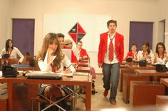 a group of young people sitting at desks in front of a man and woman