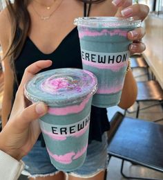 two people holding up cups with pink and blue toppings on them in front of a table